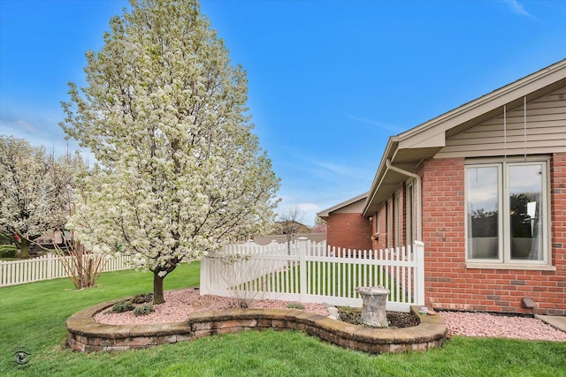 view of side of property featuring fence, a yard, and brick siding