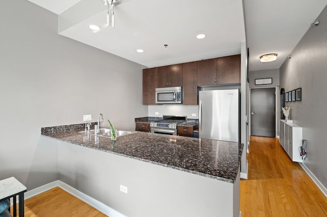 kitchen featuring dark brown cabinetry, a sink, a peninsula, stainless steel appliances, and light wood-style flooring
