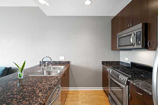 kitchen with dark brown cabinetry, a sink, baseboards, light wood finished floors, and stainless steel appliances