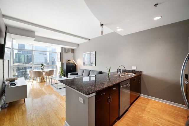 kitchen with a peninsula, baseboards, light wood-type flooring, a sink, and stainless steel appliances