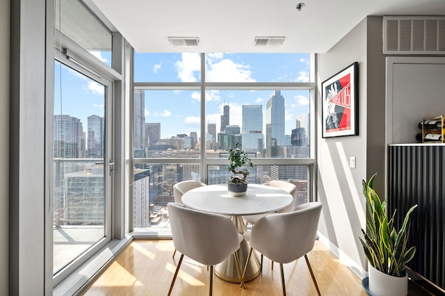 dining room featuring light wood-style floors, floor to ceiling windows, a city view, and visible vents