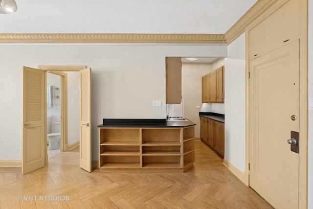 kitchen featuring brown cabinetry, dark countertops, open shelves, a sink, and baseboards