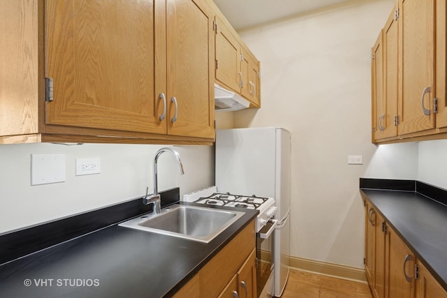 kitchen featuring dark countertops, baseboards, stainless steel gas range, a sink, and light wood-style flooring