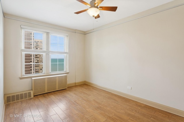 empty room with visible vents, a ceiling fan, light wood-style flooring, and radiator