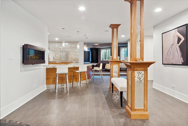 interior space with baseboards, hanging light fixtures, wood finished floors, and decorative columns