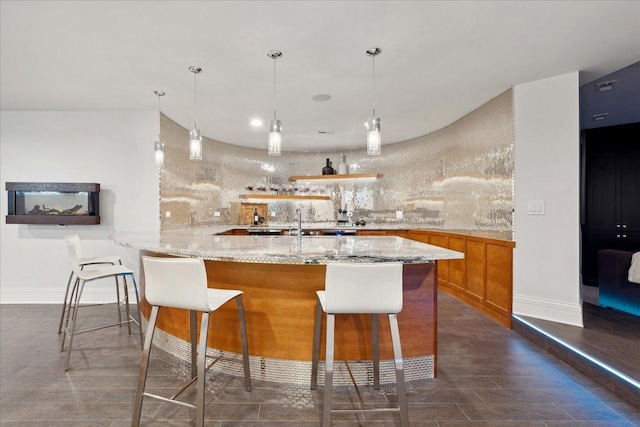 kitchen with light stone counters, a breakfast bar, a peninsula, brown cabinetry, and hanging light fixtures