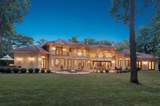 rear view of house with a chimney, a lawn, a balcony, a patio, and stucco siding