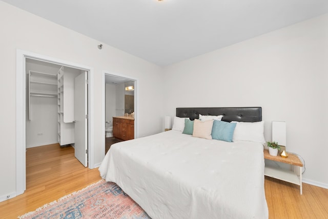 bedroom with ensuite bath, baseboards, a spacious closet, and light wood-type flooring