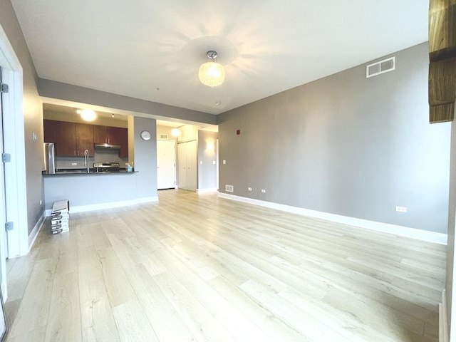 unfurnished living room featuring light wood-style floors, baseboards, and a sink