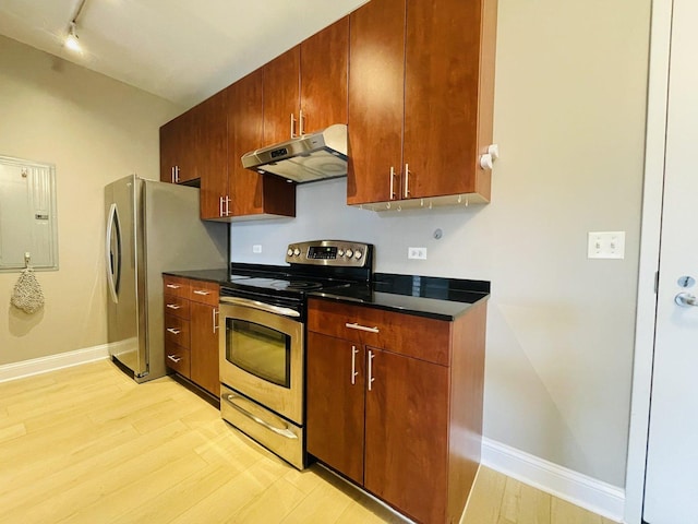 kitchen featuring stainless steel appliances, under cabinet range hood, light wood-style floors, rail lighting, and dark countertops