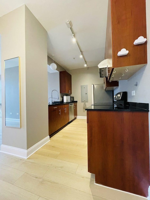kitchen featuring appliances with stainless steel finishes, rail lighting, dark countertops, baseboards, and a sink