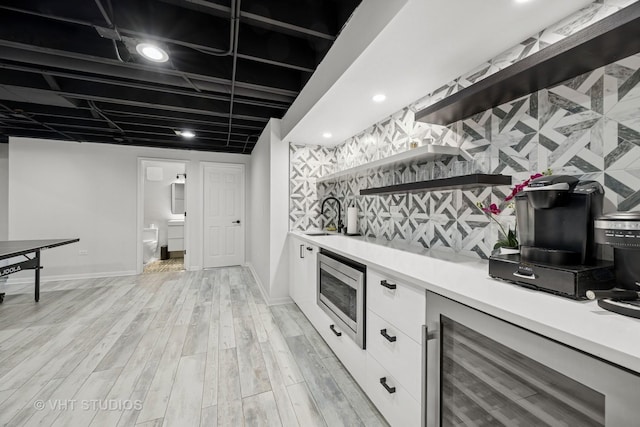 bar featuring stainless steel microwave, a sink, a dry bar, light wood-type flooring, and beverage cooler