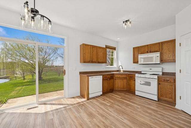 kitchen featuring white appliances, light wood-type flooring, brown cabinetry, and a sink