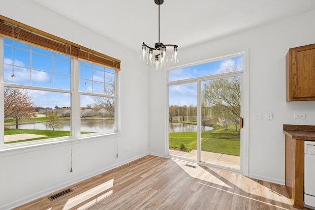 unfurnished dining area with light wood finished floors, visible vents, a notable chandelier, and a water view