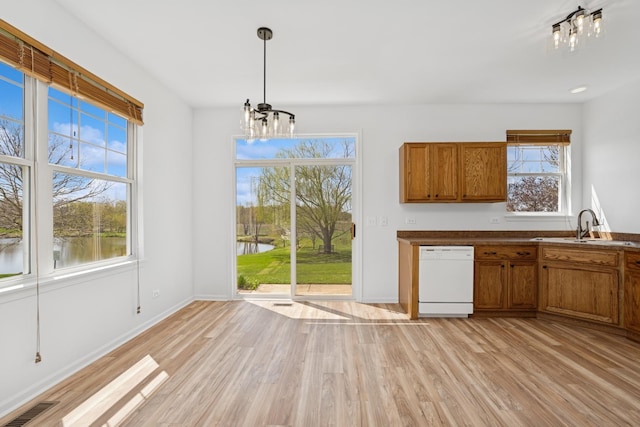 unfurnished dining area featuring a sink, plenty of natural light, an inviting chandelier, and light wood-type flooring