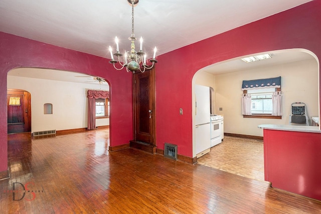unfurnished dining area featuring visible vents, arched walkways, ceiling fan with notable chandelier, and hardwood / wood-style flooring