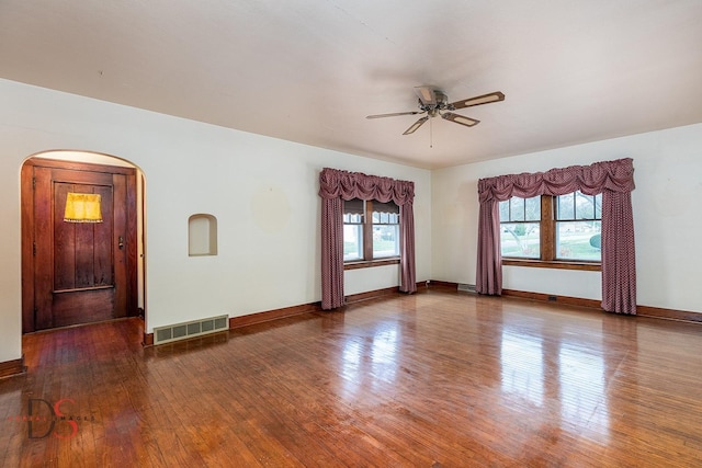 unfurnished room with ceiling fan, visible vents, arched walkways, wood finished floors, and baseboards