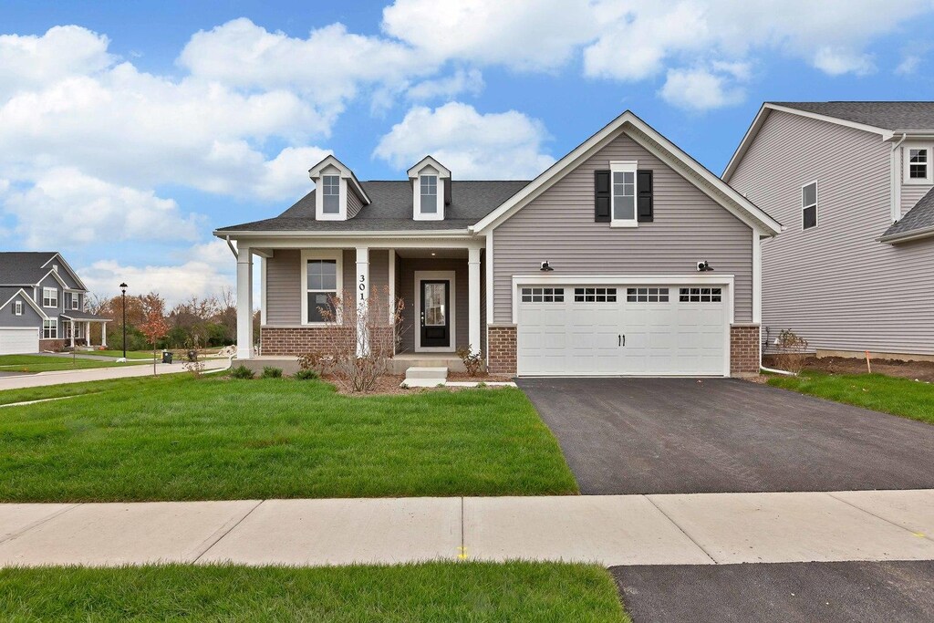 view of front of property featuring a front lawn, an attached garage, driveway, a porch, and brick siding