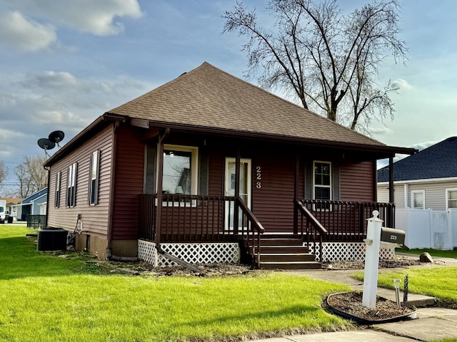 bungalow-style home featuring central AC unit, a front lawn, a shingled roof, and covered porch