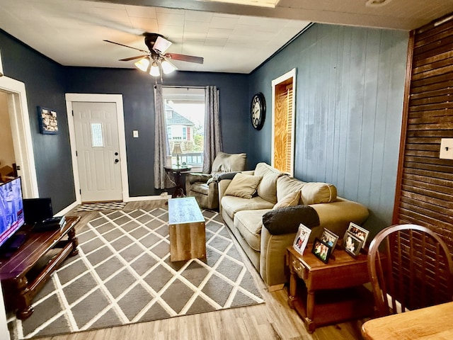 living room featuring wood finished floors, wood walls, baseboards, and ceiling fan