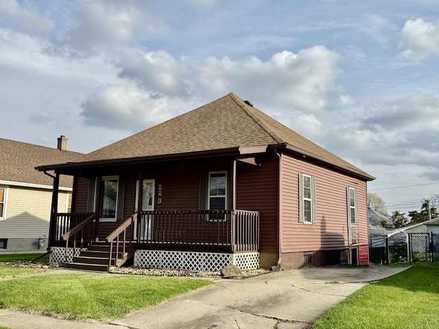 view of front of house with fence, covered porch, a front lawn, and roof with shingles