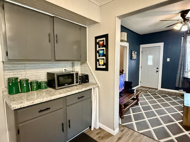 interior space with wood finished floors, stainless steel microwave, baseboards, tasteful backsplash, and ceiling fan