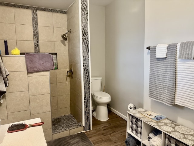 bathroom with toilet, baseboards, wood finished floors, and a tile shower