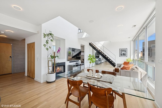 dining space featuring visible vents, wood finished floors, a warm lit fireplace, and stairway