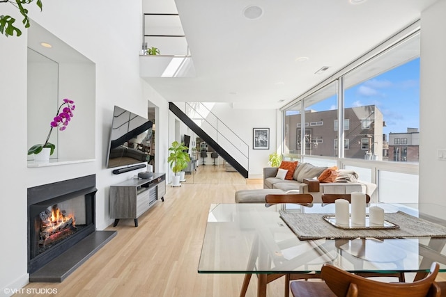 living area featuring a wall of windows, a warm lit fireplace, light wood-style floors, and stairway