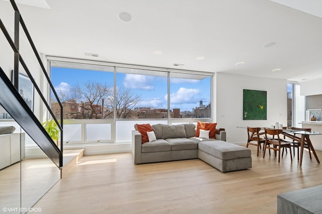 living room with floor to ceiling windows, stairway, a healthy amount of sunlight, and light wood finished floors