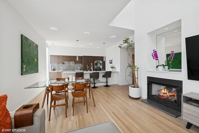 dining space with recessed lighting, a warm lit fireplace, light wood finished floors, and baseboards