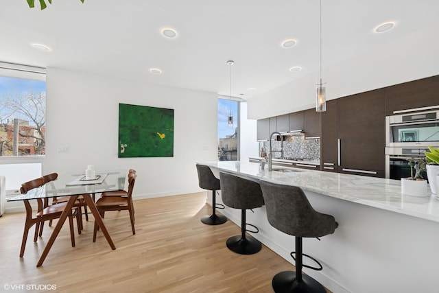 kitchen with light stone counters, decorative backsplash, light wood-style flooring, a kitchen bar, and decorative light fixtures