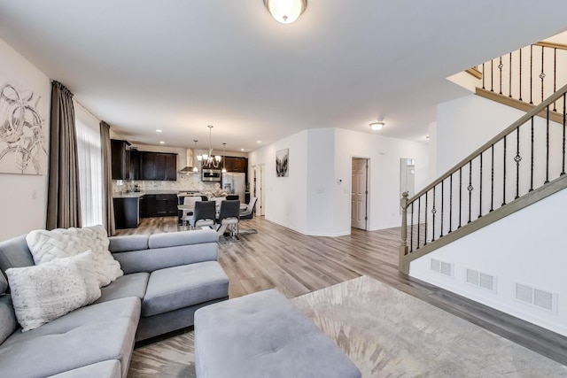 living room with stairway, an inviting chandelier, light wood-style floors, and visible vents
