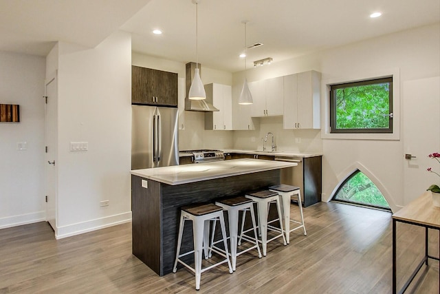 kitchen with wall chimney exhaust hood, stainless steel appliances, a sink, wood finished floors, and a breakfast bar area