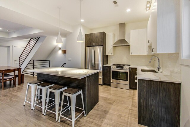 kitchen featuring light wood-type flooring, a breakfast bar, wall chimney exhaust hood, stainless steel appliances, and a sink