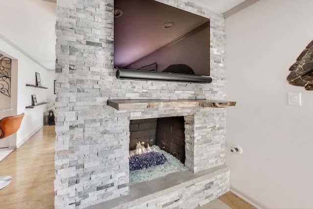 room details with a stone fireplace, baseboards, and wood finished floors