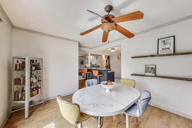 dining room with baseboards, ceiling fan, ornamental molding, and light wood-style flooring