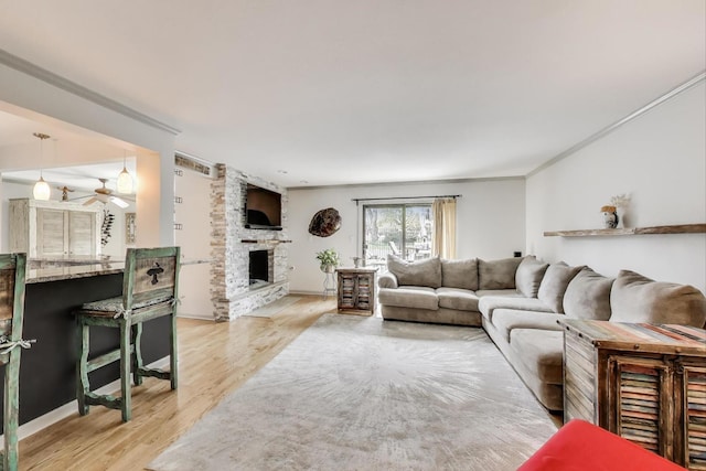 living area with crown molding, ceiling fan, a fireplace, and light wood-type flooring