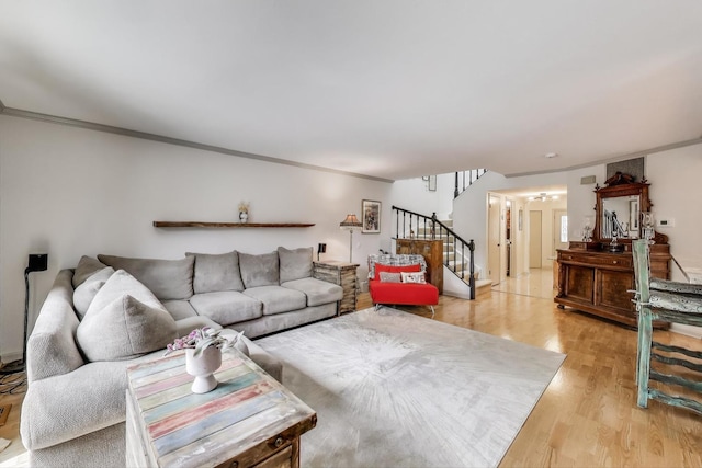 living area featuring crown molding, light wood-style flooring, and stairs