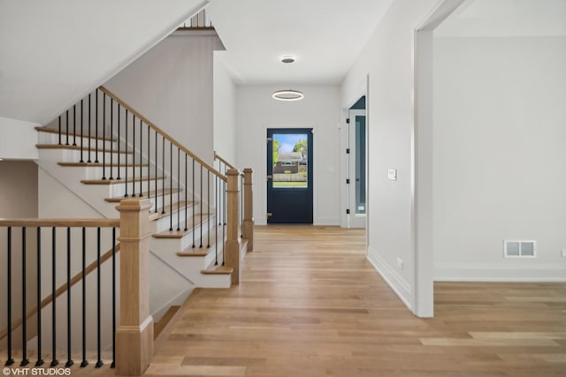 entryway with wood finished floors, visible vents, baseboards, and stairs