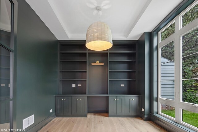 interior space featuring wood finished floors, built in shelves, a tray ceiling, baseboards, and visible vents