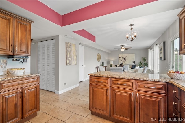 kitchen featuring light tile patterned flooring, light stone countertops, brown cabinetry, and ceiling fan with notable chandelier