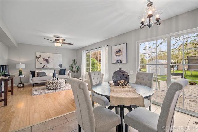 dining space featuring light tile patterned floors, baseboards, and ceiling fan with notable chandelier