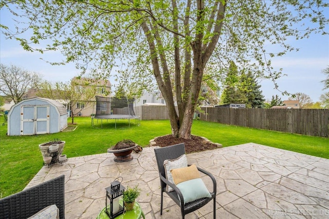 view of patio featuring a trampoline, an outbuilding, a fenced backyard, an outdoor fire pit, and a storage unit