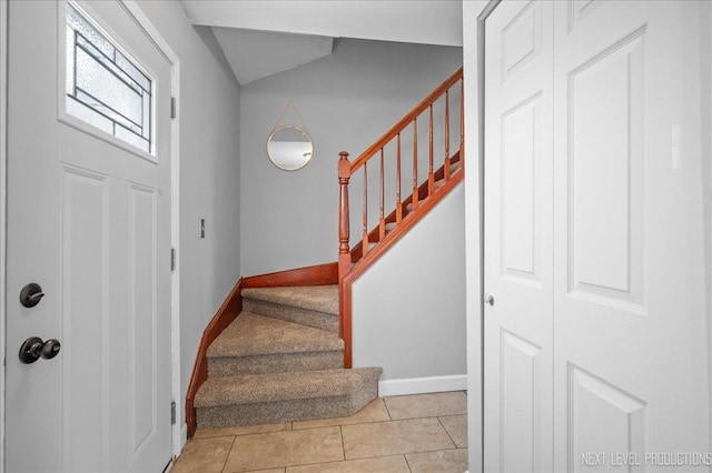 foyer entrance with baseboards, light tile patterned floors, and stairway