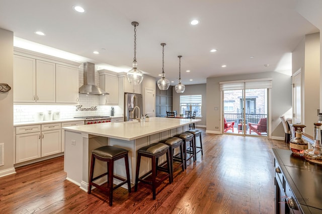 kitchen with a sink, stainless steel fridge, wall chimney range hood, a breakfast bar, and an island with sink