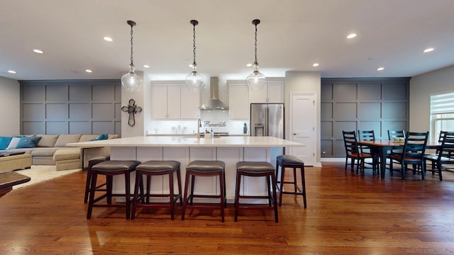 kitchen with wall chimney range hood, tasteful backsplash, an island with sink, a breakfast bar area, and high quality fridge