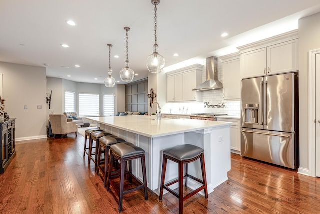 kitchen featuring recessed lighting, a breakfast bar, backsplash, wall chimney exhaust hood, and appliances with stainless steel finishes