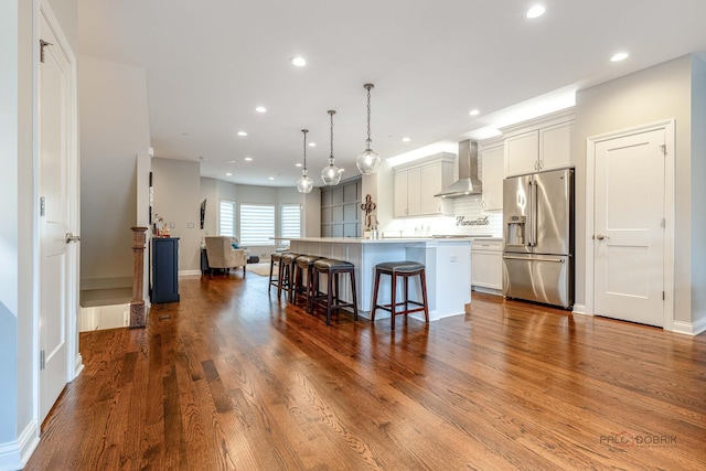 kitchen featuring a kitchen breakfast bar, high end fridge, a kitchen island with sink, wall chimney exhaust hood, and recessed lighting