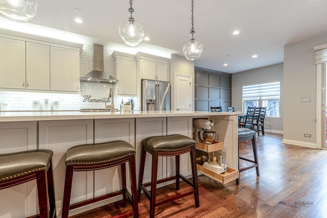 kitchen with a breakfast bar, high end fridge, backsplash, wall chimney exhaust hood, and baseboards